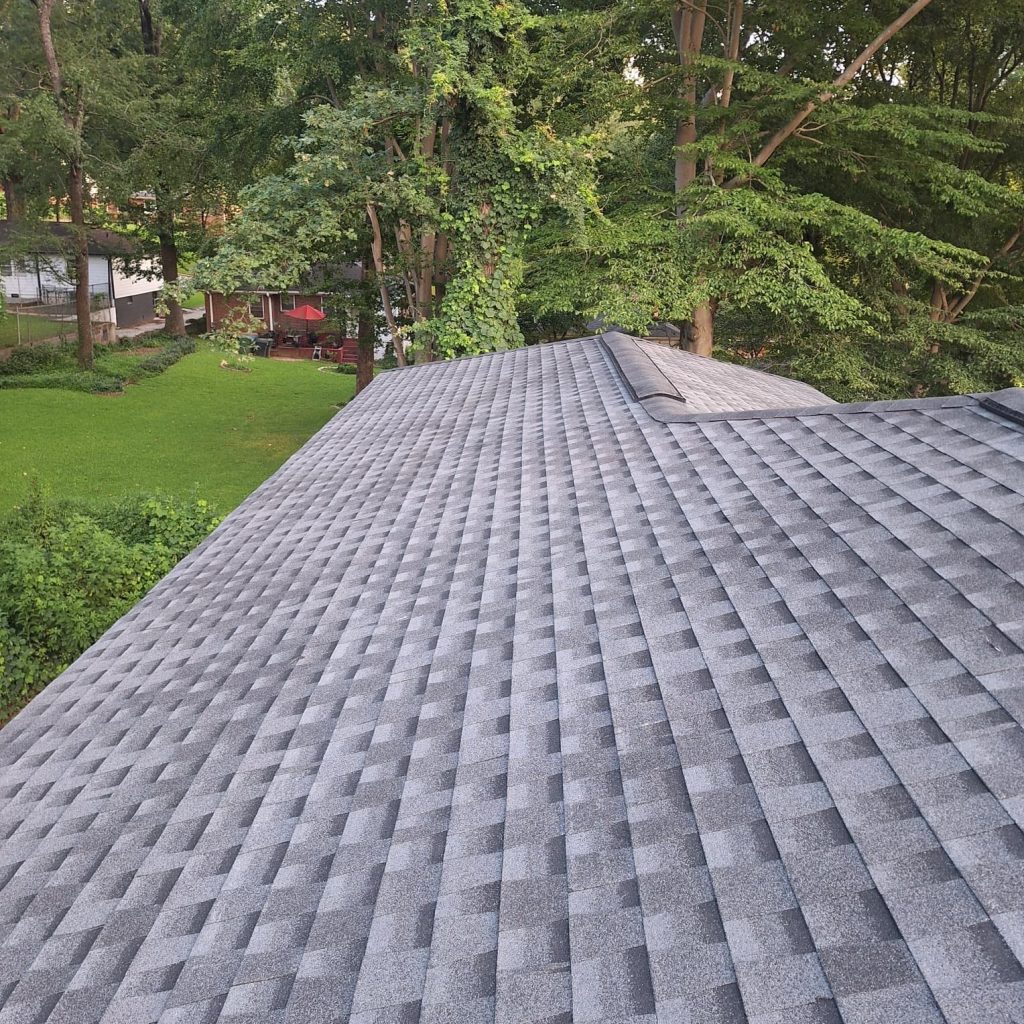 Gray asphalt shingle roof installation in green residential area surrounded by trees, showcasing HD Pro Roofing expertise.
