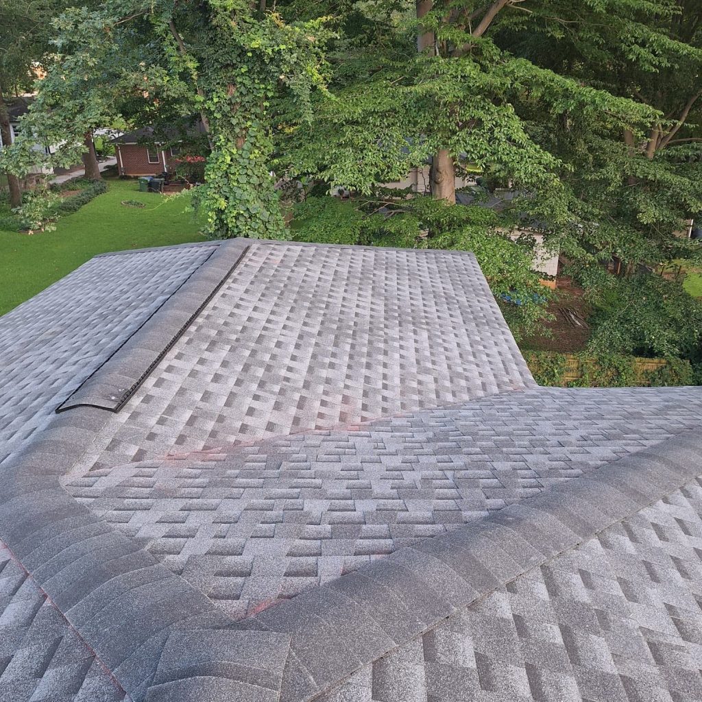 Gray asphalt shingle roof with ridge vent surrounded by lush green trees, installed professionally by HD Pro Roofing.
