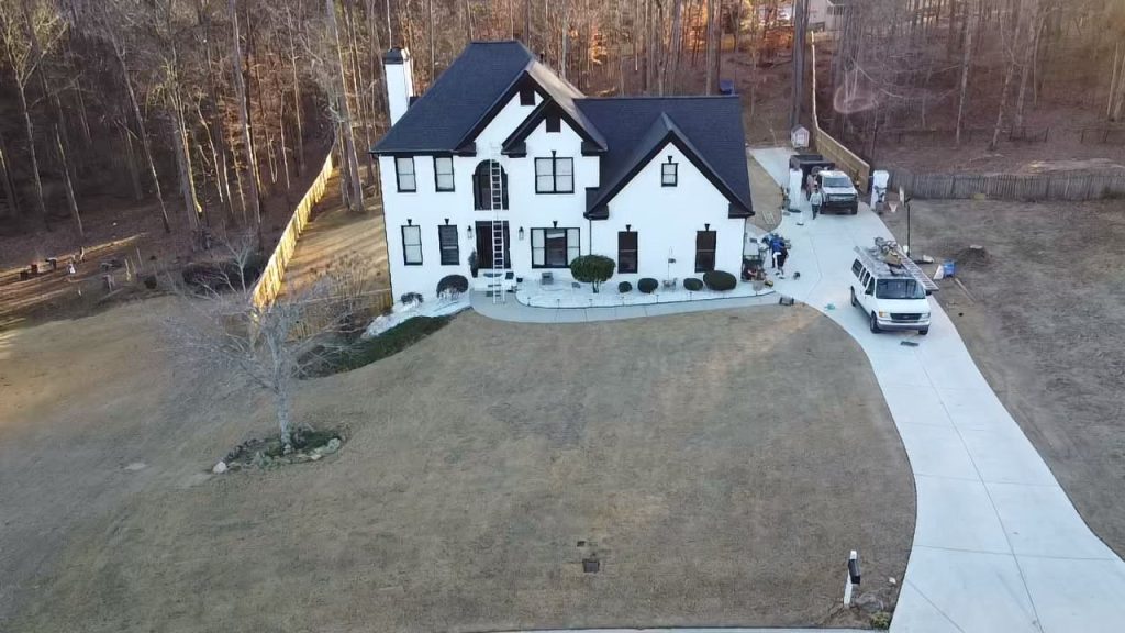 White house with black roofing, surrounded by trees, roofing team with equipment and vehicle near driveway, HD Pro Roofing service.
