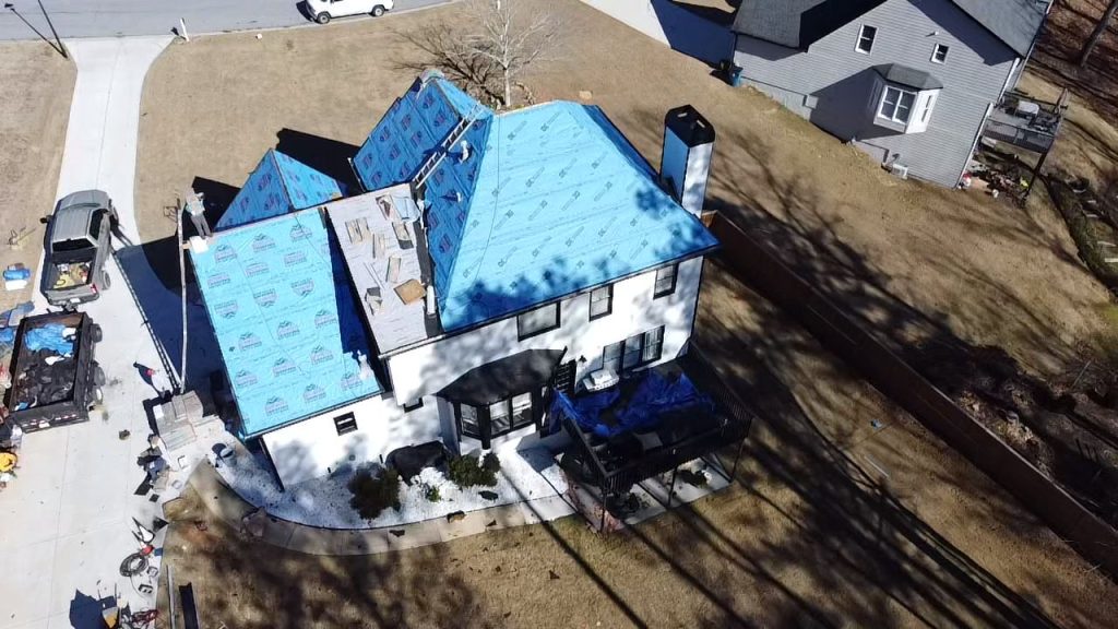 Aerial view of house roof installation with blue HD Pro Roofing underlayment, workers, tools, and equipment in residential area