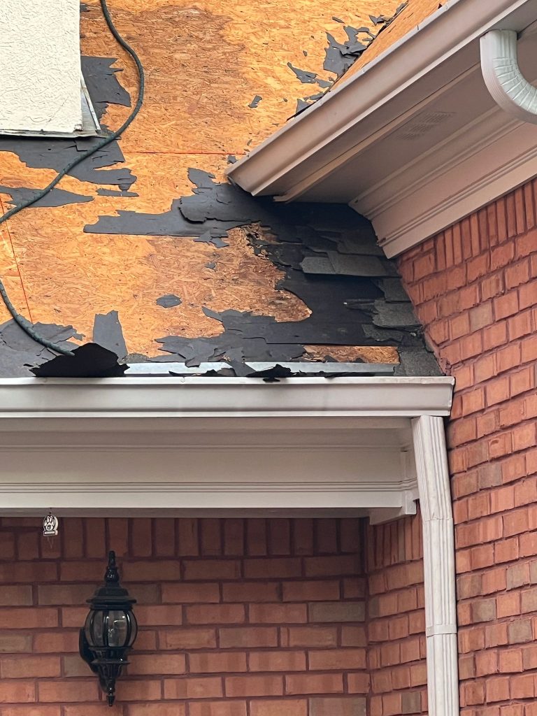 Damaged roof with torn shingles exposing wood deck on red-brick house. Issues include missing shingles and roof wear, HD Pro Roofing.