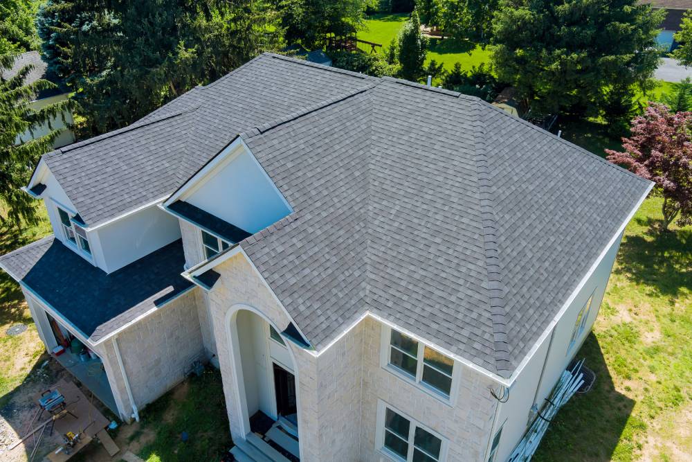 Newly installed black asphalt shingle roof on two-story home by HD Pro Roofing, surrounded by trees and greenery.